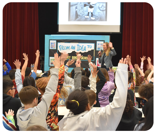 Lowey Bundy Sichol presenting to an auditorium of students. Everyone has their hands raised.