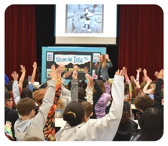 Lowey Bundy Sichol presenting to grade school children during an Author Visit. Everyone has their hand raised.