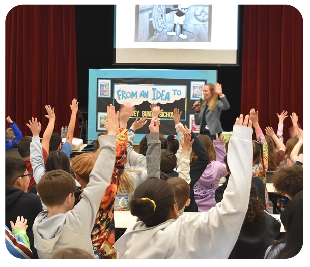 Lowey Bundy Sichol presenting to an auditorium of students. Everyone has their hands raised.