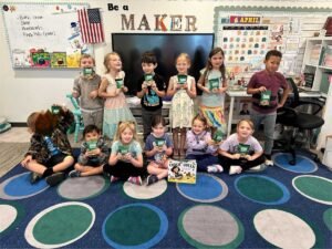 Children smiling with copies of Cookie Queen with actual cookies after a virtual meeting with Lowey Bundy Sichol.