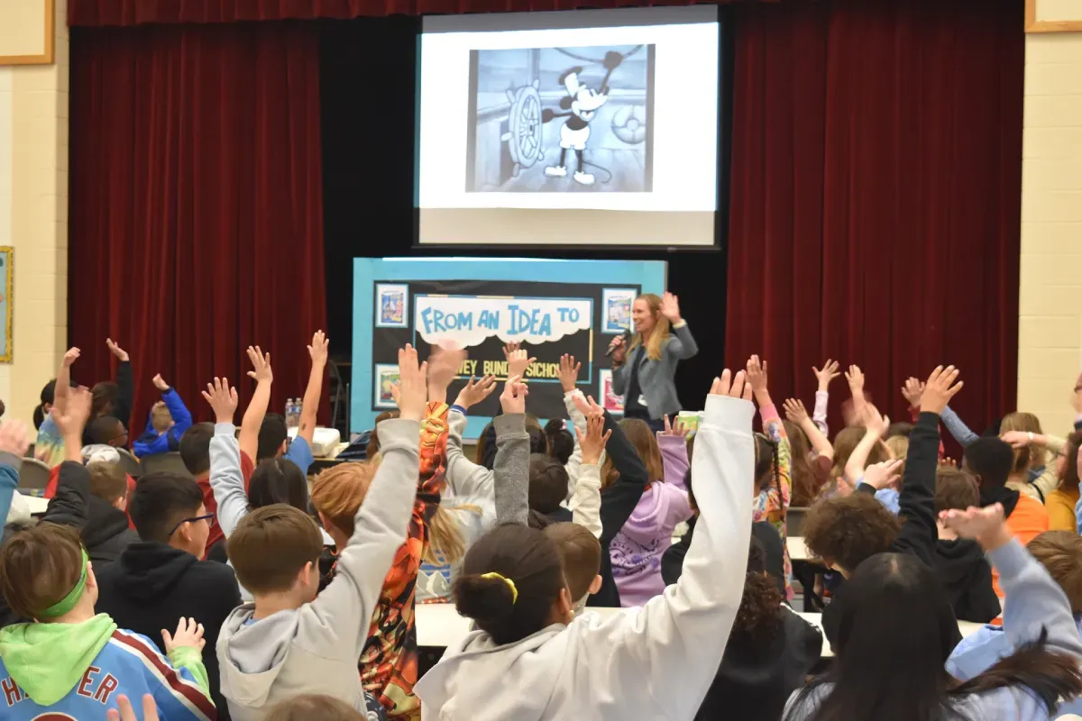 Lowey Bundy Sichol speaking to elementary school students during an author visit as children eagerly raise their hands.