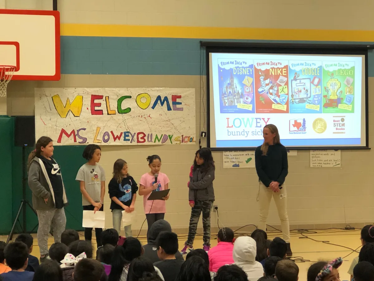 Elementary school students speaking in front of an auditorium  during an author visit from Lowey Bundy Sichol.